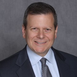 Bruce Weiss wearing a suit and tie and smiling